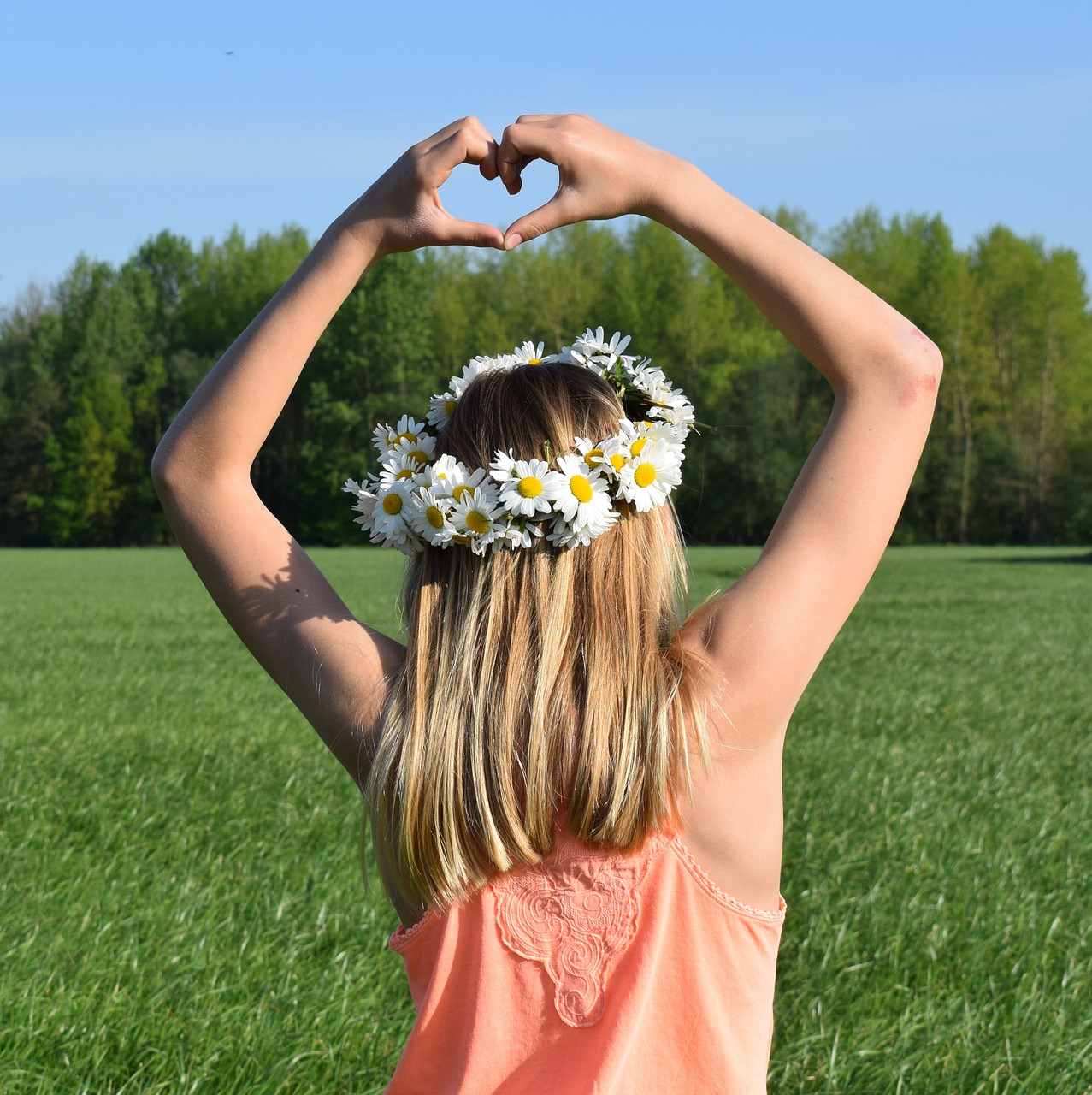Chica de espaldas con corona de flores y haciendo un corazón con las manos.